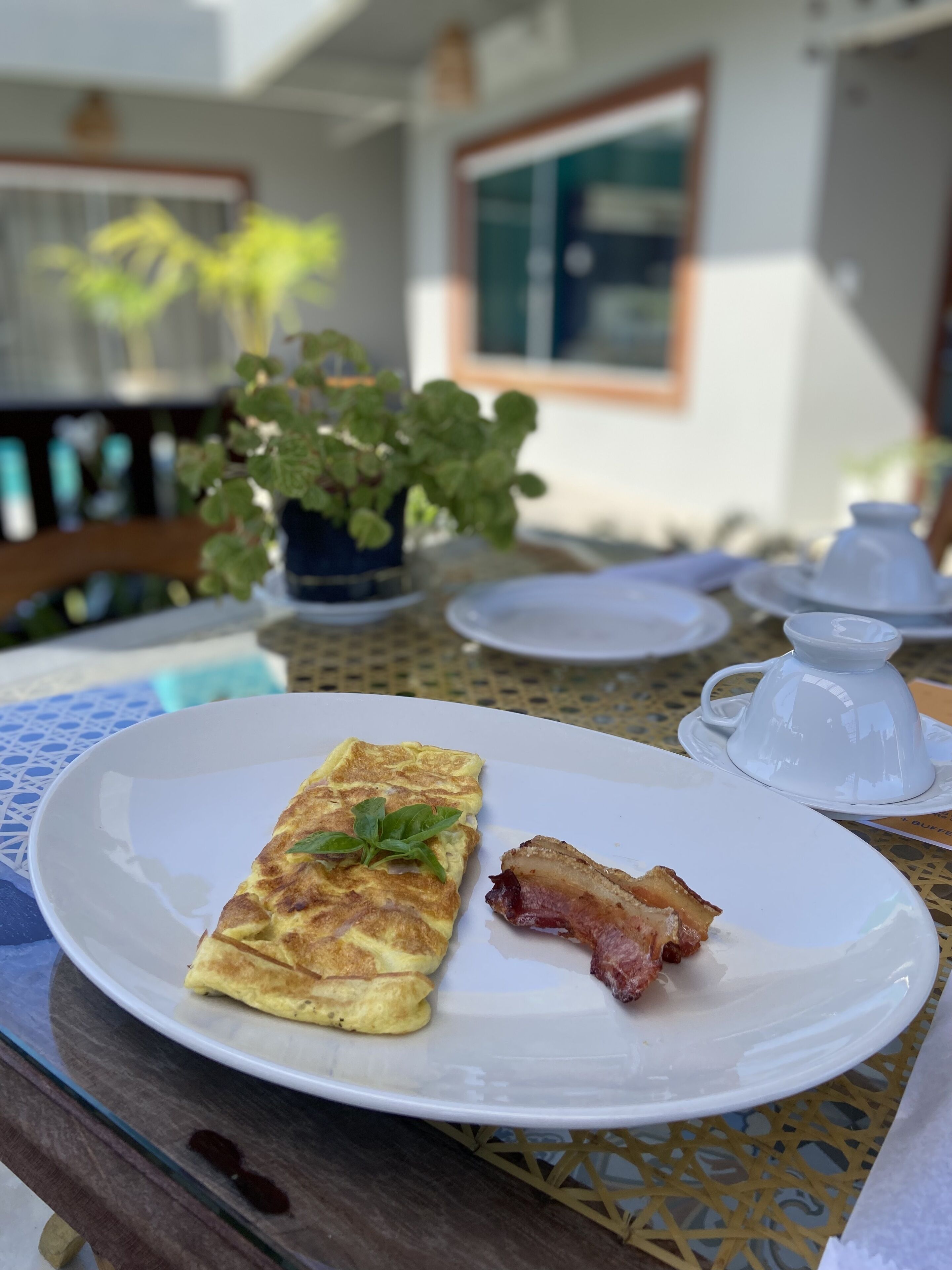 Un plato de desayuno con tortilla y tocino sobre una mesa al aire libre.