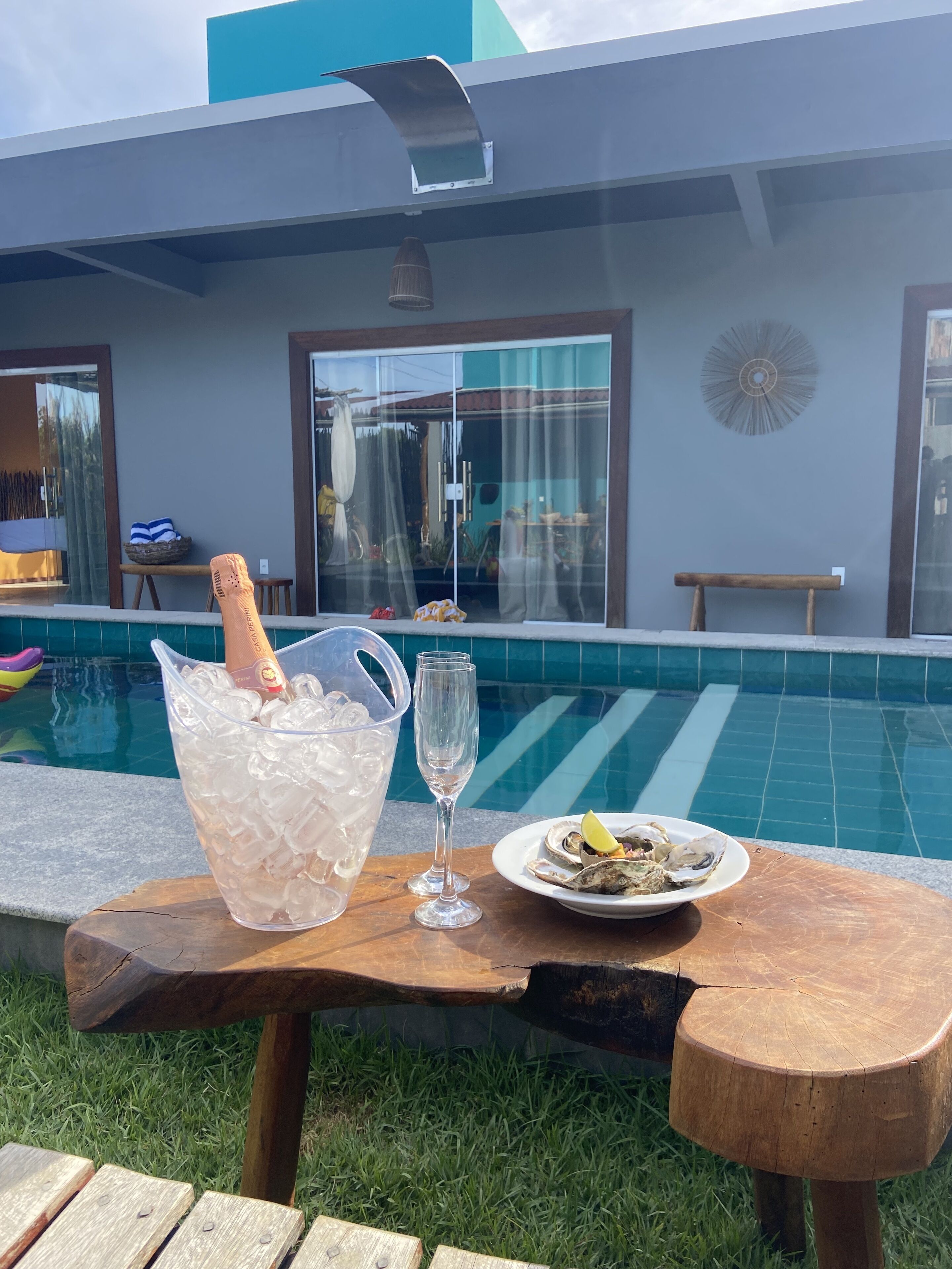 Un tavolino a bordo piscina con un drink, un piatto di ostriche e un bicchiere di champagne.