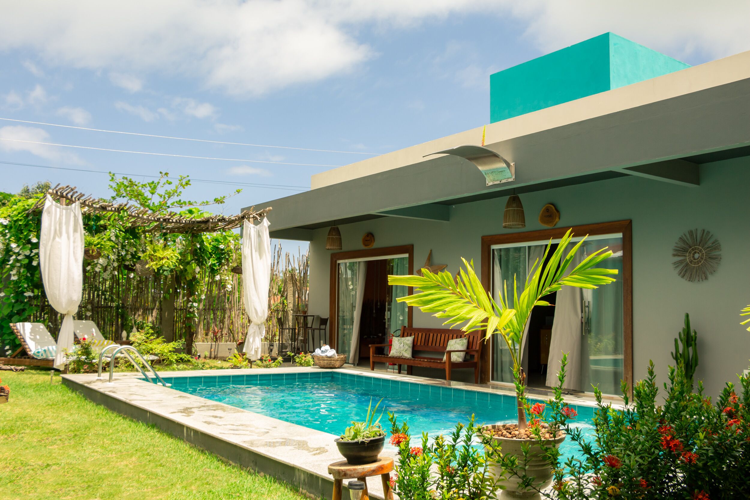 Una casa moderna con piscina, mobiliario exterior y abundante vegetación.