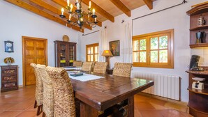 Un coin repas avec une table en bois et des chaises en osier, un lustre et une vue sur l’extérieur grâce à de grandes fenêtres.