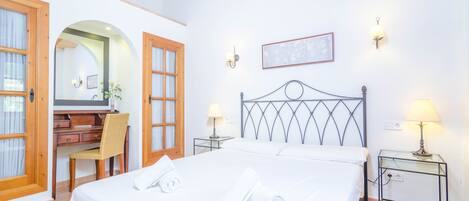 A hotel room with a bed, two bedside tables with lamps, a desk with a chair, and a large mirror.