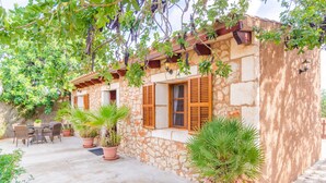 Un bâtiment en pierre avec des volets en bois, des plantes en pot et un patio aménagé avec du mobilier d’extérieur.