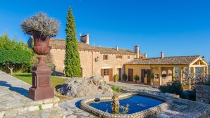 Un bâtiment en pierre doté d’une piscine, d’une pergola et d’un grand arbre.