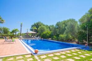 Una piscina rectangular con borde de azulejos, rodeada por una terraza con sillones de descanso y un pequeño pabellón.