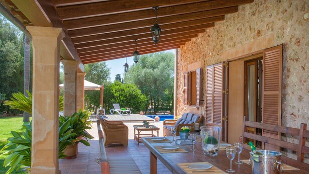 Un patio techado al aire libre con mobiliario de madera, una piscina y un muro de piedra.