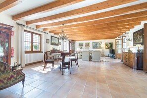 A spacious dining area with wooden beams, a chandelier, and a large window.