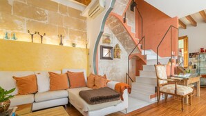 A modern living room with a white sofa, orange cushions, a wooden coffee table, and a staircase with a checkered chair.