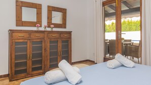 A room with a bed, two wooden cabinets with glass doors, a mirror, and a view of outdoor furniture through a glass door. - MURTA 26 - Villa with private pool in SA COMA. Free WiFi (Sant Llorenç des Cardassar)