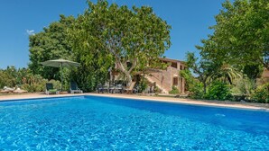 A clear blue pool with lounge chairs and an umbrella, surrounded by lush greenery and a building with a stone facade. - CAN SUA - Beautiful rustic finca with private pool, located a few km from the beach Free W (Artà)