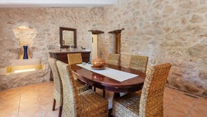 A dining area with a stone wall, a wooden table, wicker chairs, and a large vase. - CAN SUA - Beautiful rustic finca with private pool, located a few km from the beach Free W (Artà)
