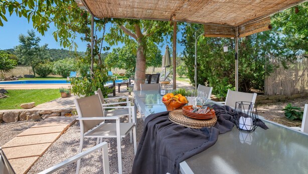 An outdoor patio with a glass table, white chairs, a woven umbrella, and a pool in the background. - CAN SUA - Beautiful rustic finca with private pool, located a few km from the beach Free W (Artà)