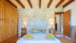 A bedroom with a stone wall, wooden wardrobe, bed with colorful towels, and two bedside tables with lamps. - CAN SUA - Beautiful rustic finca with private pool, located a few km from the beach Free W (Artà)