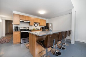A modern kitchen with wooden cabinets, a stainless steel refrigerator, and a central island with bar stools. - 5102 Peters · Large loft near Kings Island. On bike trail/River. (Maineville)