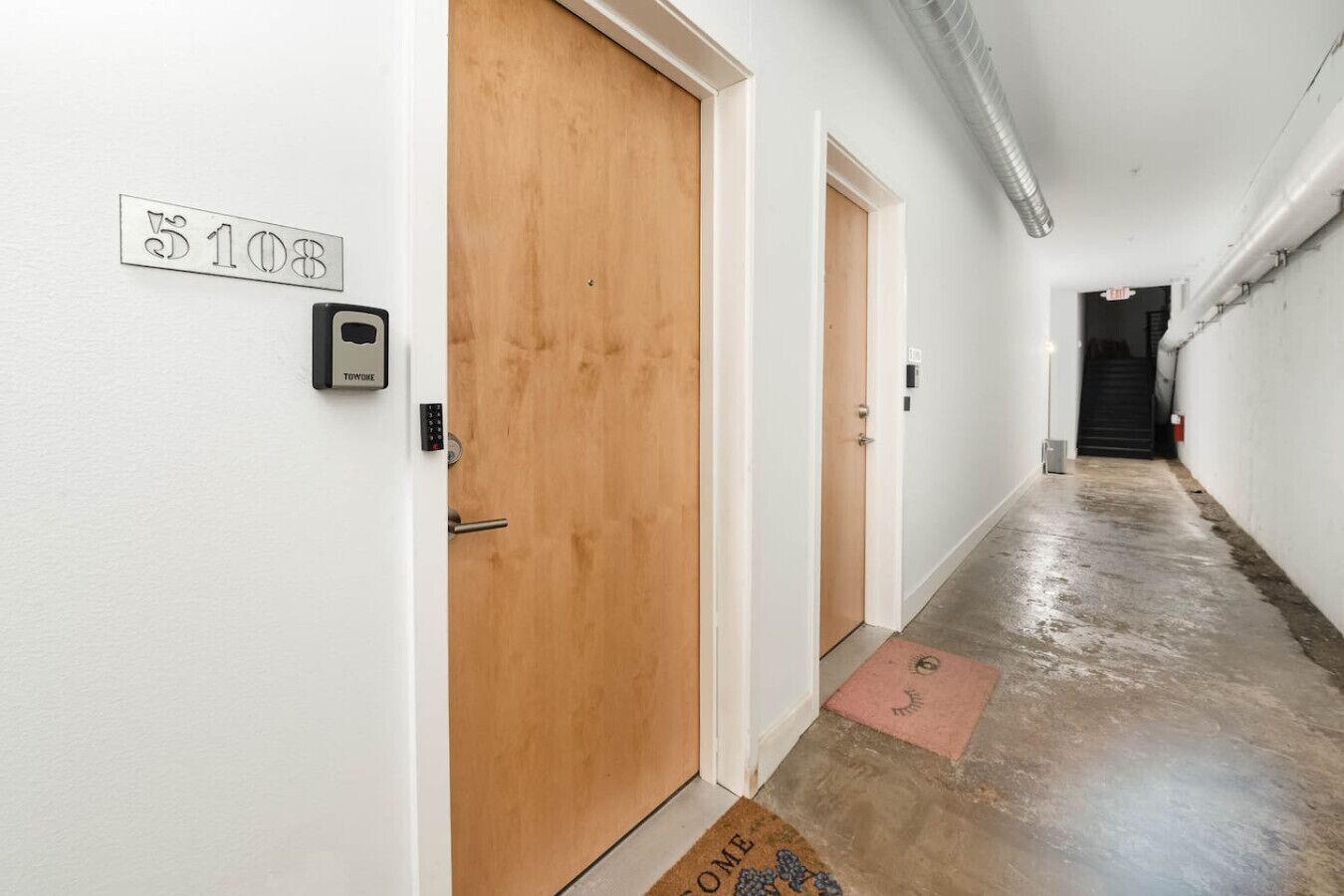 Un couloir avec une porte en bois, une serrure électronique et un paillasson.