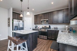A modern kitchen with dark wood cabinets, granite countertops, stainless steel appliances, and pendant lighting. - 5738 Azra Court · Cheerful 5 bedroom on azra with a pool and real (Morrow)