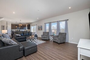 A modern living room with a sofa set, armchairs, and a coffee table. There is a kitchen area with cabinets and a dining table. - 5738 Azra Court · Cheerful 5 bedroom on azra with a pool and real (Morrow)