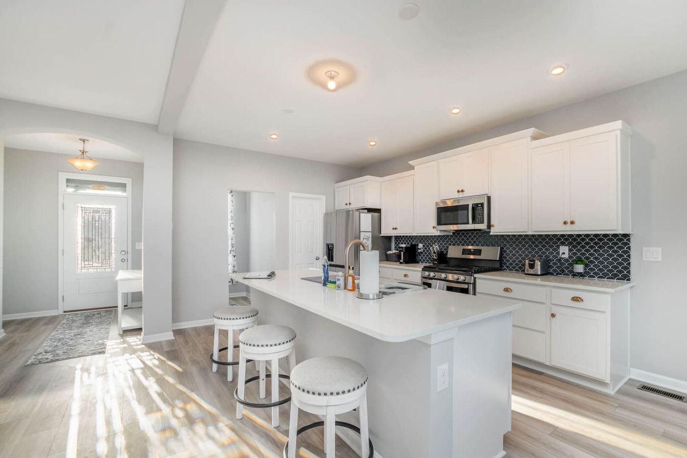 A modern kitchen with white cabinetry, a central island with stools, stainless steel appliances, and a patterned backsplash.