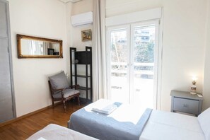 A bedroom with a bed, a chair, a nightstand, a mirror, and a window with a view of buildings. - Amazing apartment at Exarcheia (Athens)