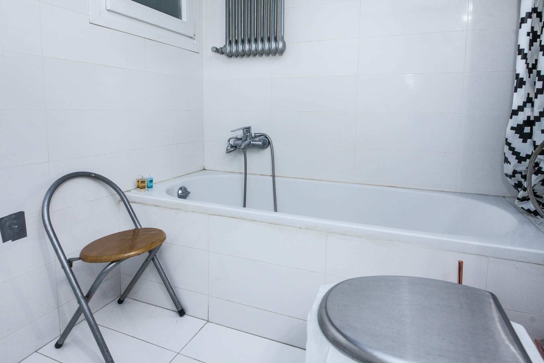 A bathroom with a white tiled floor, a bathtub, a shower, a toilet, and a chair.