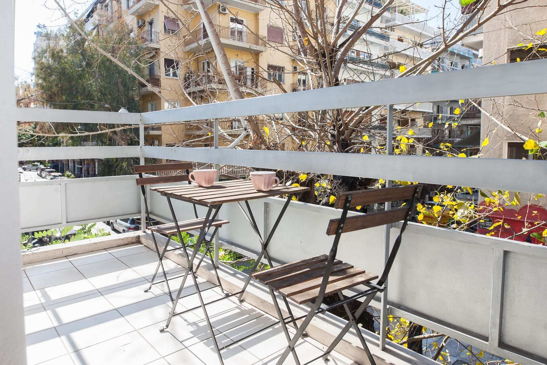A balcony with a table and two chairs, overlooking a residential area with buildings and trees.