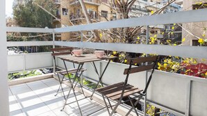 A balcony with a table and two chairs, overlooking a residential area with buildings and trees.