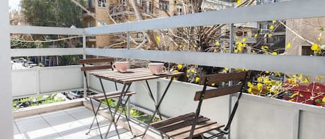 A balcony with a table and two chairs, overlooking a residential area with buildings and trees.