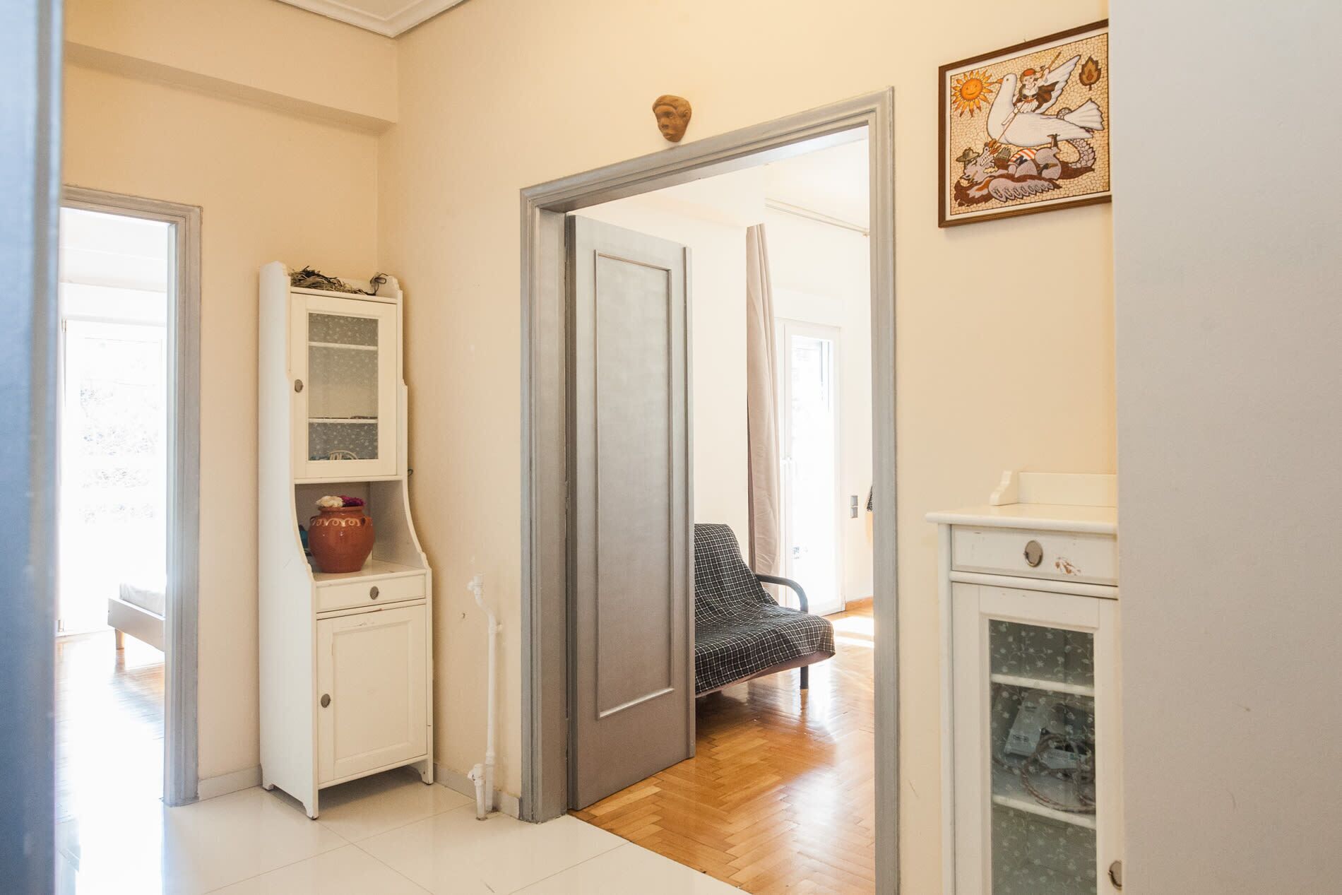 A hallway with a white cabinet, a checkered chair, and a door leading to another room.