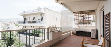 Un balcone con una sedia di legno, vista sui palazzi vicini e pavimento piastrellato.