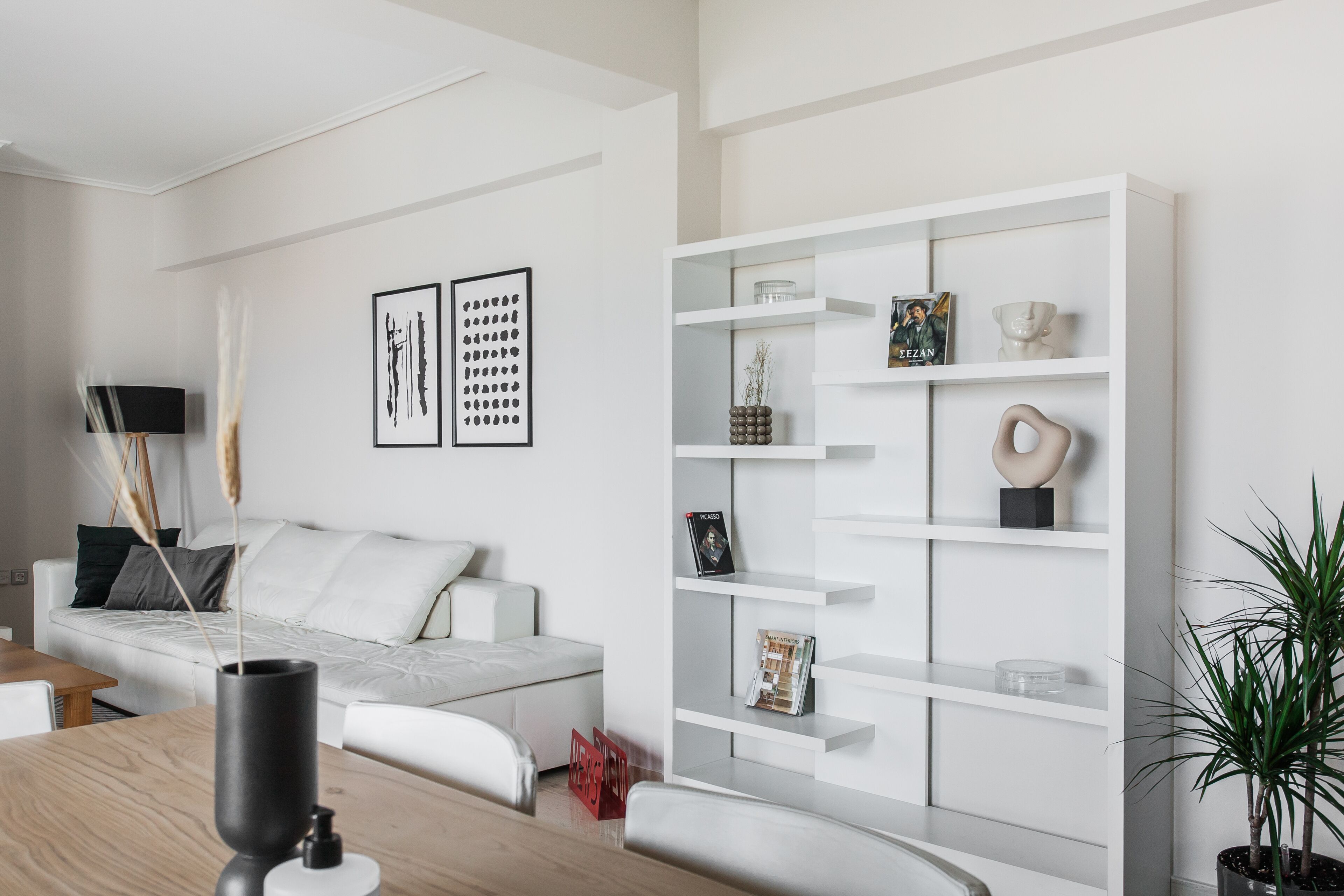 A modern living room with a white sofa, a white shelving unit, and a potted plant.