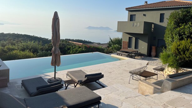 Una villa moderna con piscina, mobiliario exterior y vistas al mar y las colinas.
