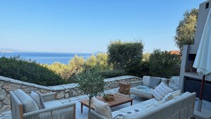Un área de estar al aire libre con mobiliario de mimbre, piso de piedra y vista al mar.