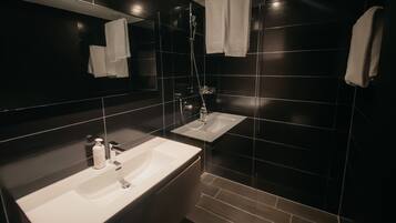 Ein modernes Badezimmer mit dunklen Fliesen, zwei Waschbecken, einem Spiegel und einer Dusche.