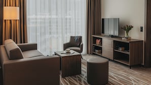 A modern hotel room with a sofa, a coffee table, a TV, and a bookshelf. - IIP Apartments - Self Check In (Spreitenbach)