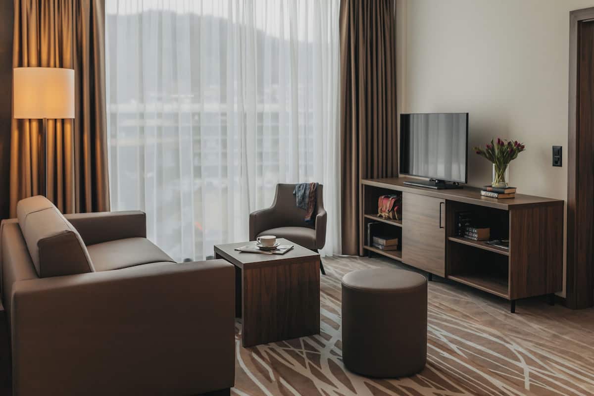 A modern hotel room with a sofa, a coffee table, a TV, and a bookshelf.