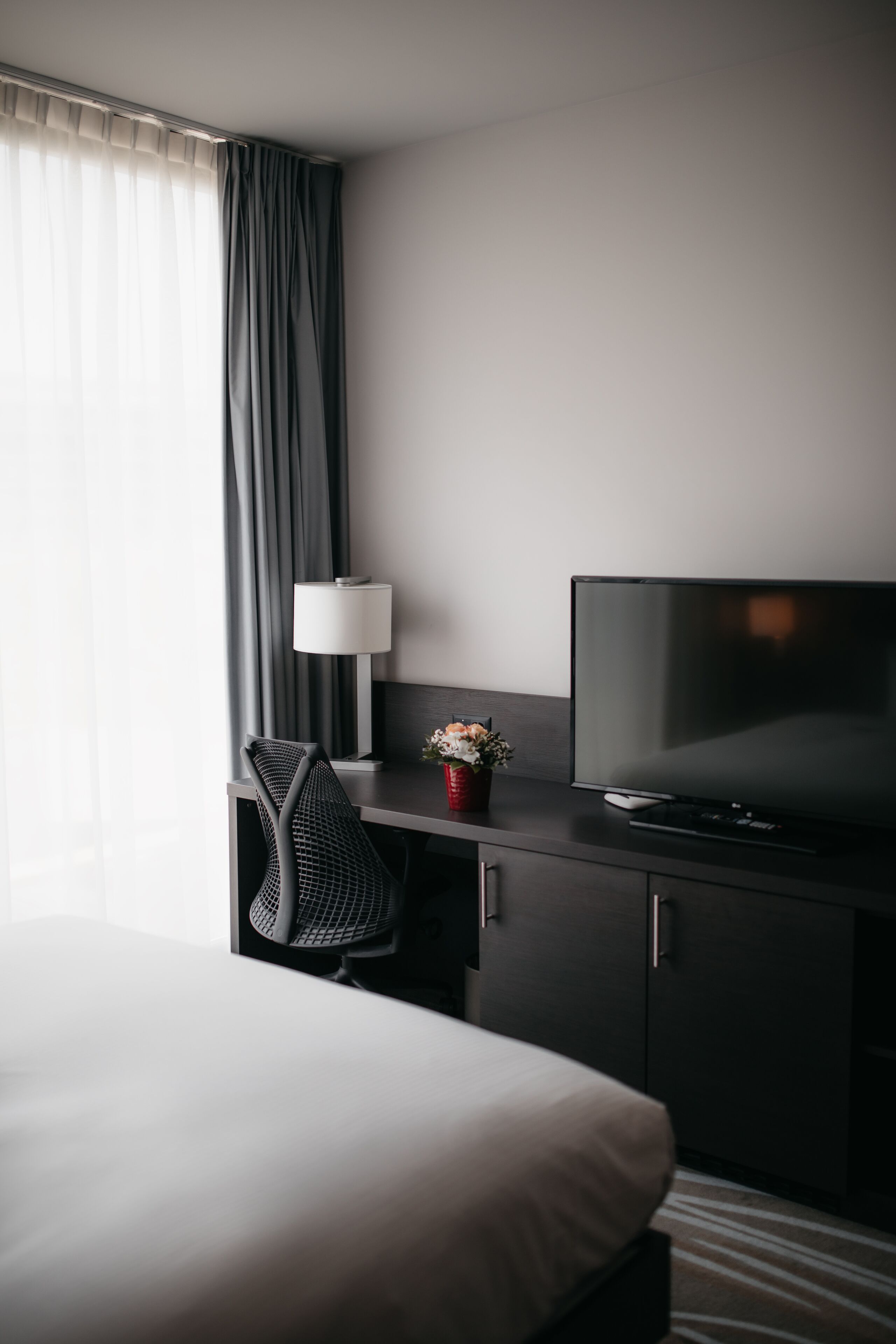 A hotel room with a bed, a desk with a television, a lamp, and a chair.