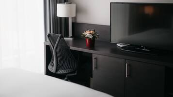 A hotel room with a bed, a desk with a television, a lamp, and a chair.