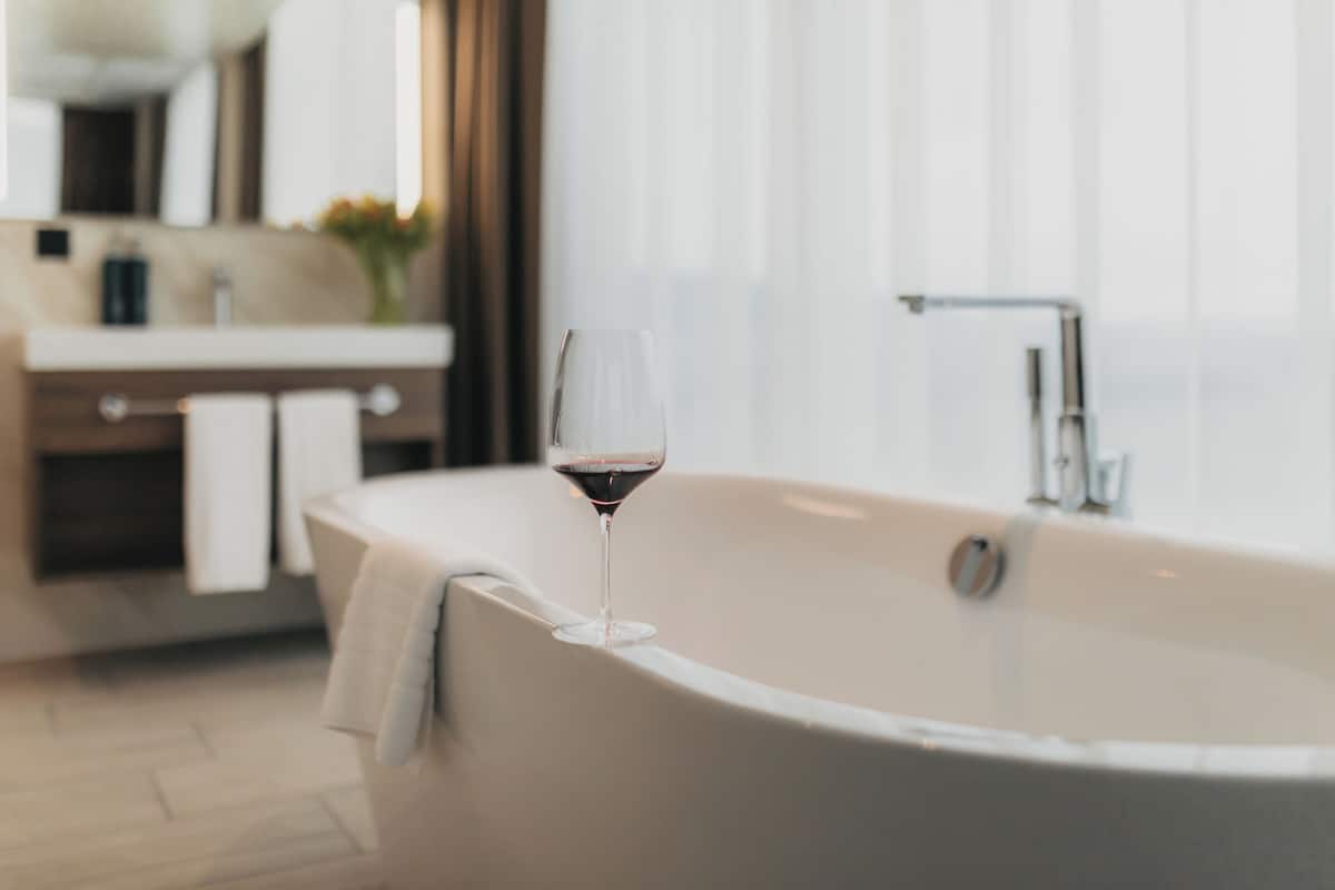 A modern bathroom with a freestanding bathtub, a glass of red wine, and a towel hanging on the side.