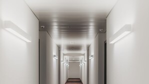 A long, narrow hallway with a patterned carpet and white walls. - IIP Apartments - Self Check In (Spreitenbach)
