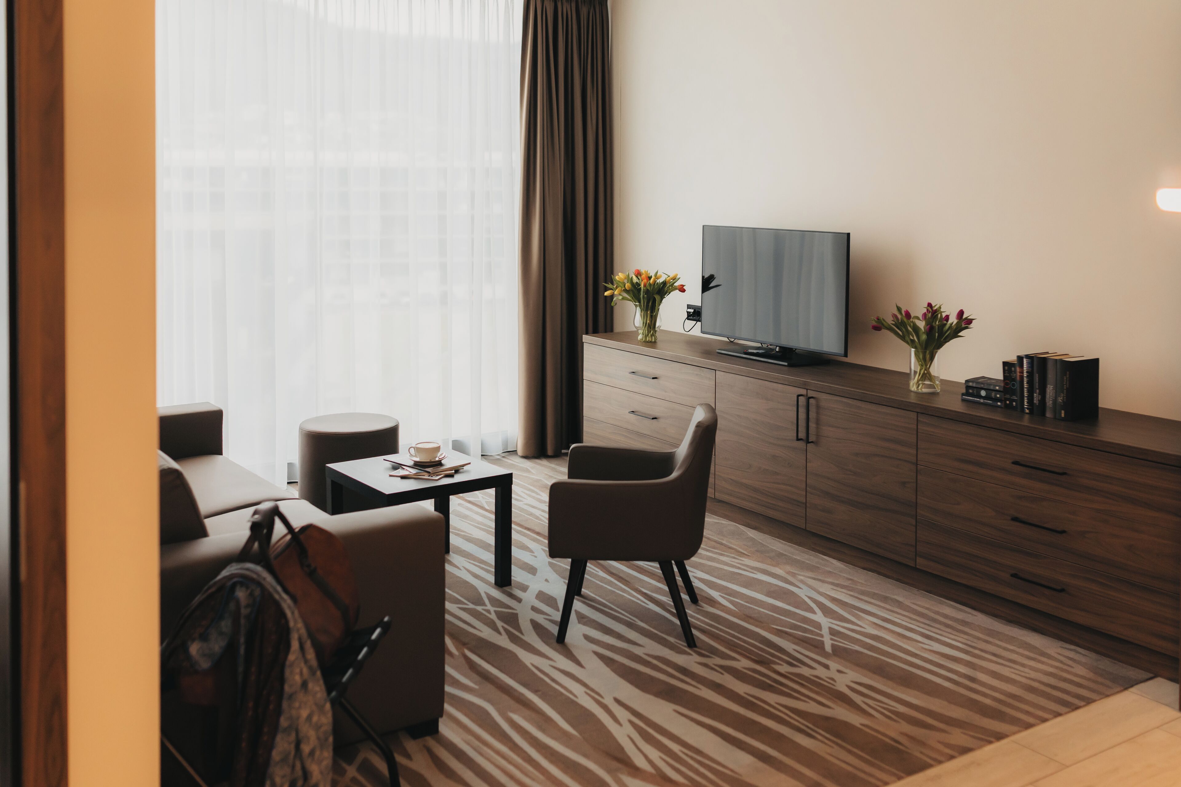 Een moderne hotelkamer met een bank, een salontafel, een televisie op een houten kast en een kamerkleed met dessin.