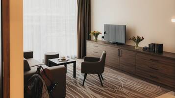 Een moderne hotelkamer met een bank, een salontafel, een televisie op een houten kast en een kamerkleed met dessin.