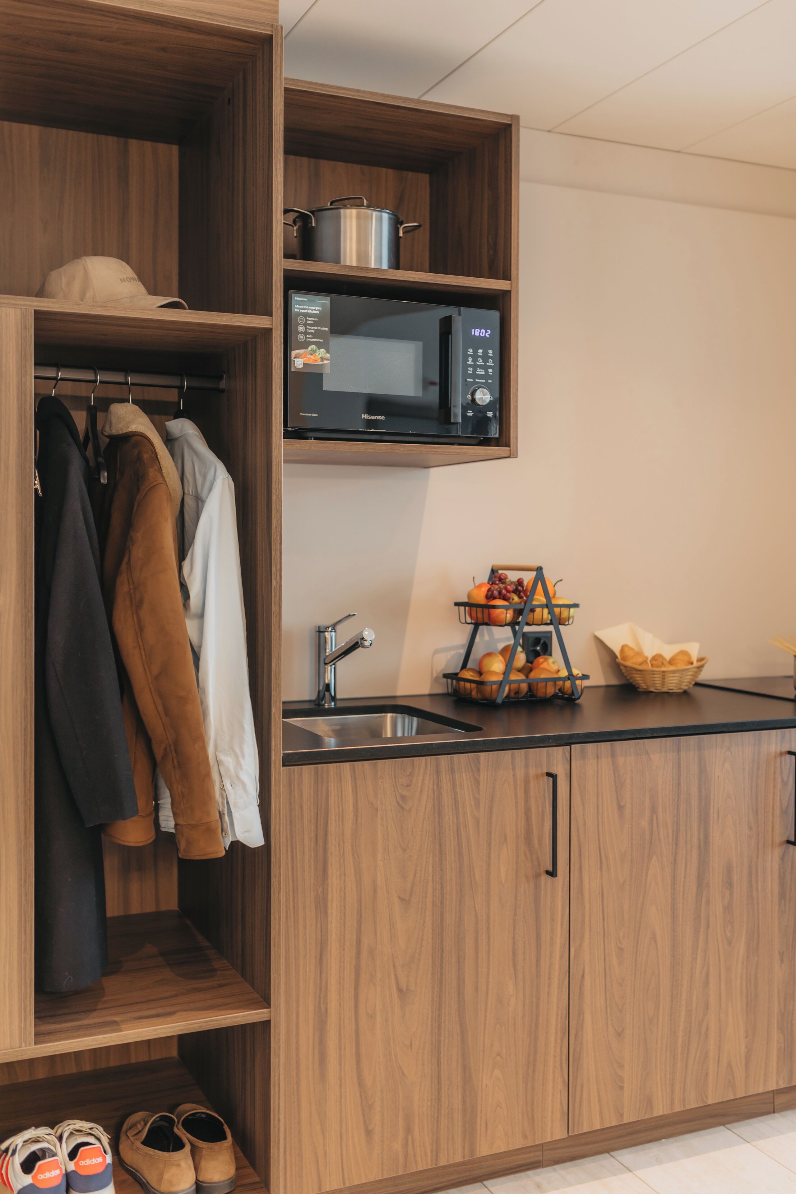 A compact kitchen with wooden cabinetry, a microwave, a sink, and a fruit basket.
