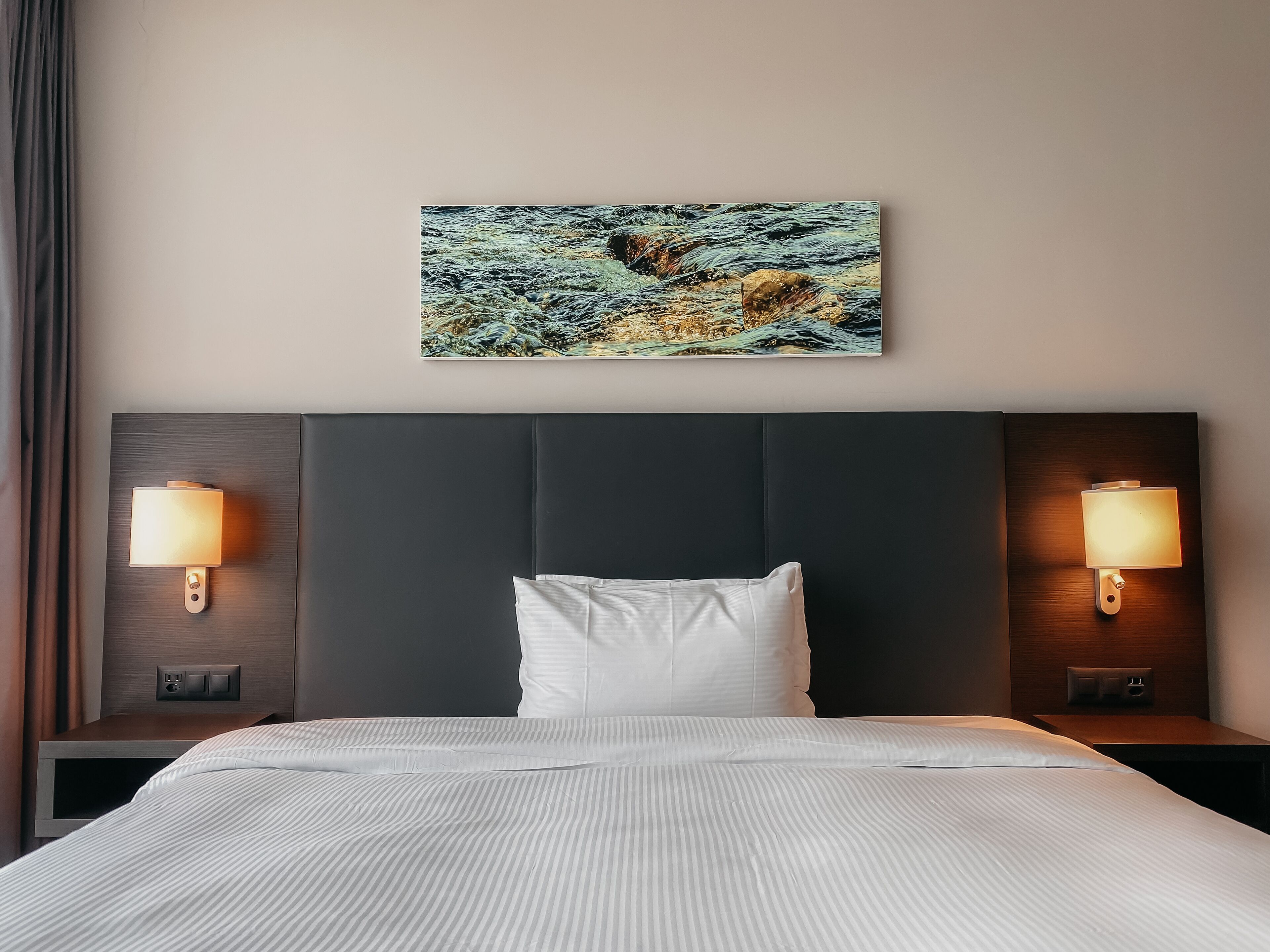 Ein Hotelzimmer mit einem großen Bett, zwei Nachttischlampen, einem Kopfteil und einem Gemälde an der Wand.