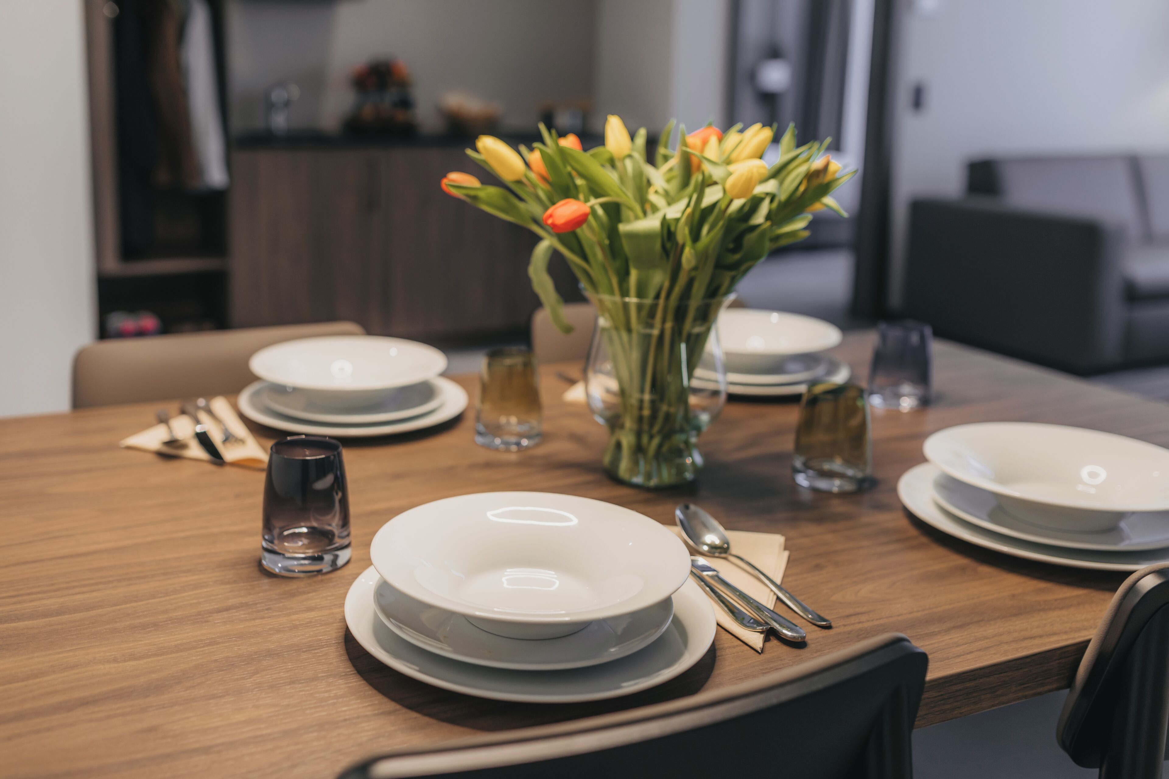 A dining table set with plates, cutlery, and a vase of flowers.
