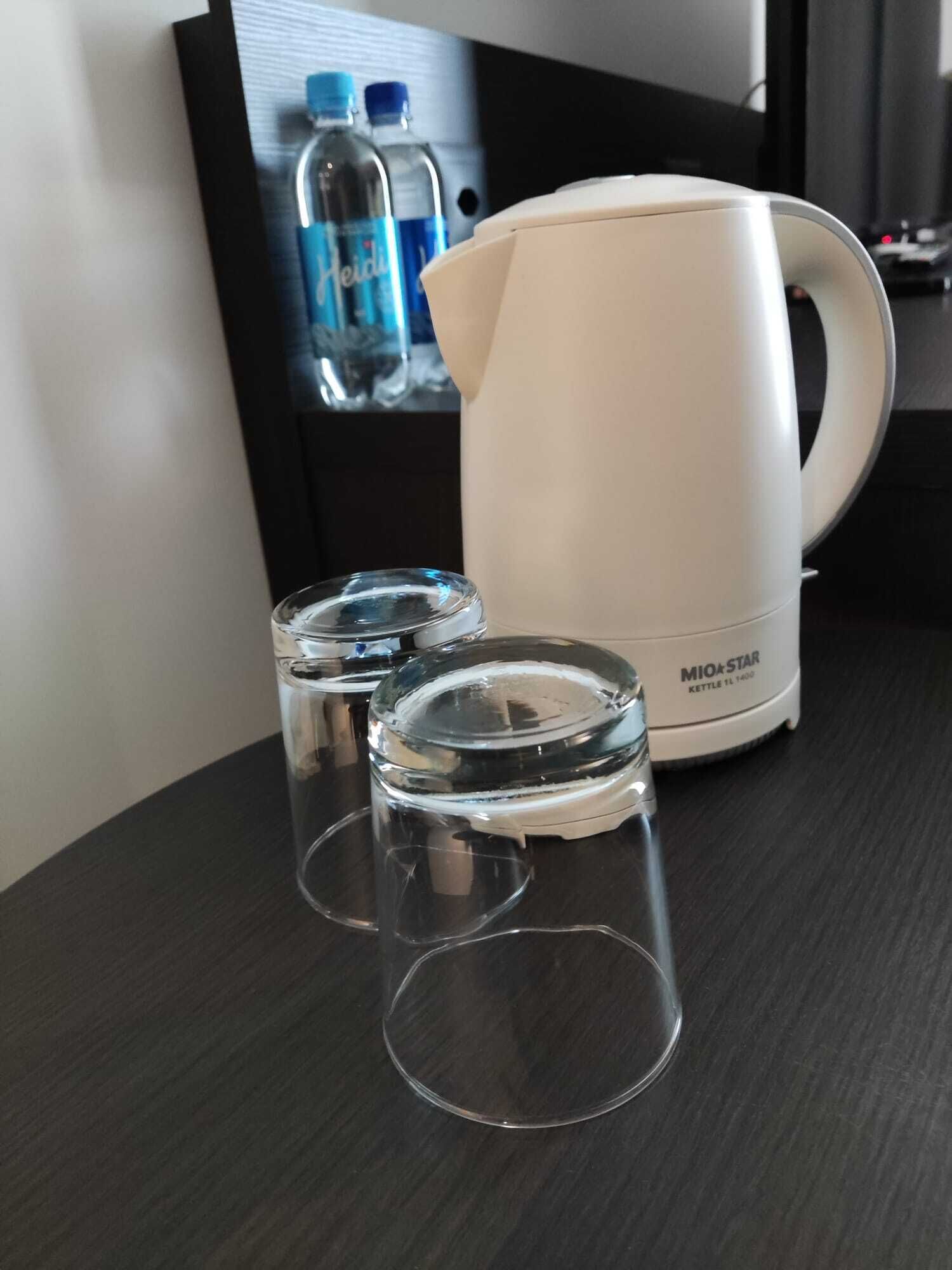 A white MIO+STAR kettle on a dark wooden table with two clear glasses.