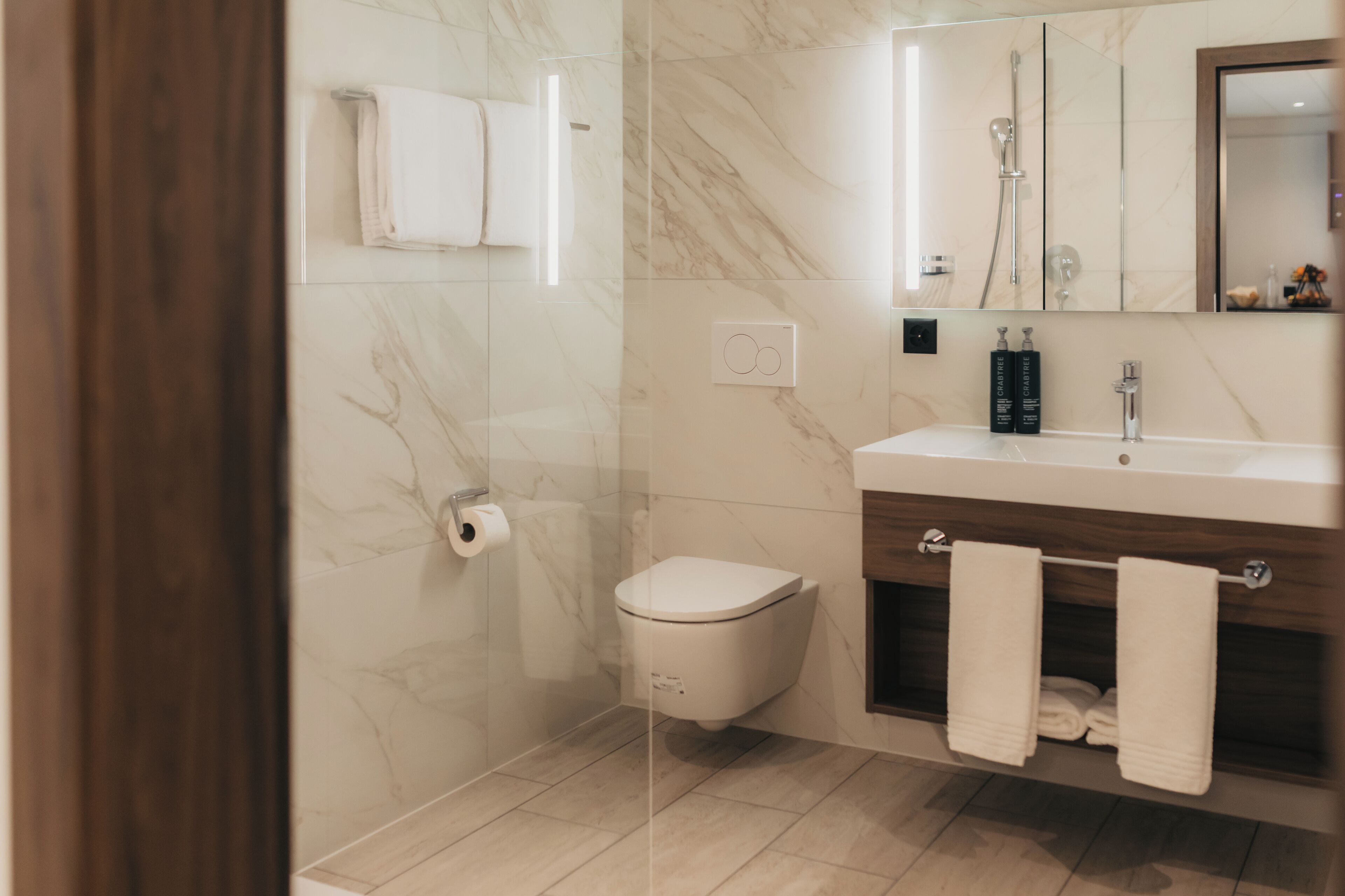 A modern bathroom with a toilet, a glass-enclosed shower, a vanity with a mirror, and a towel rack.