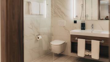 A modern bathroom with a toilet, a glass-enclosed shower, a vanity with a mirror, and a towel rack.