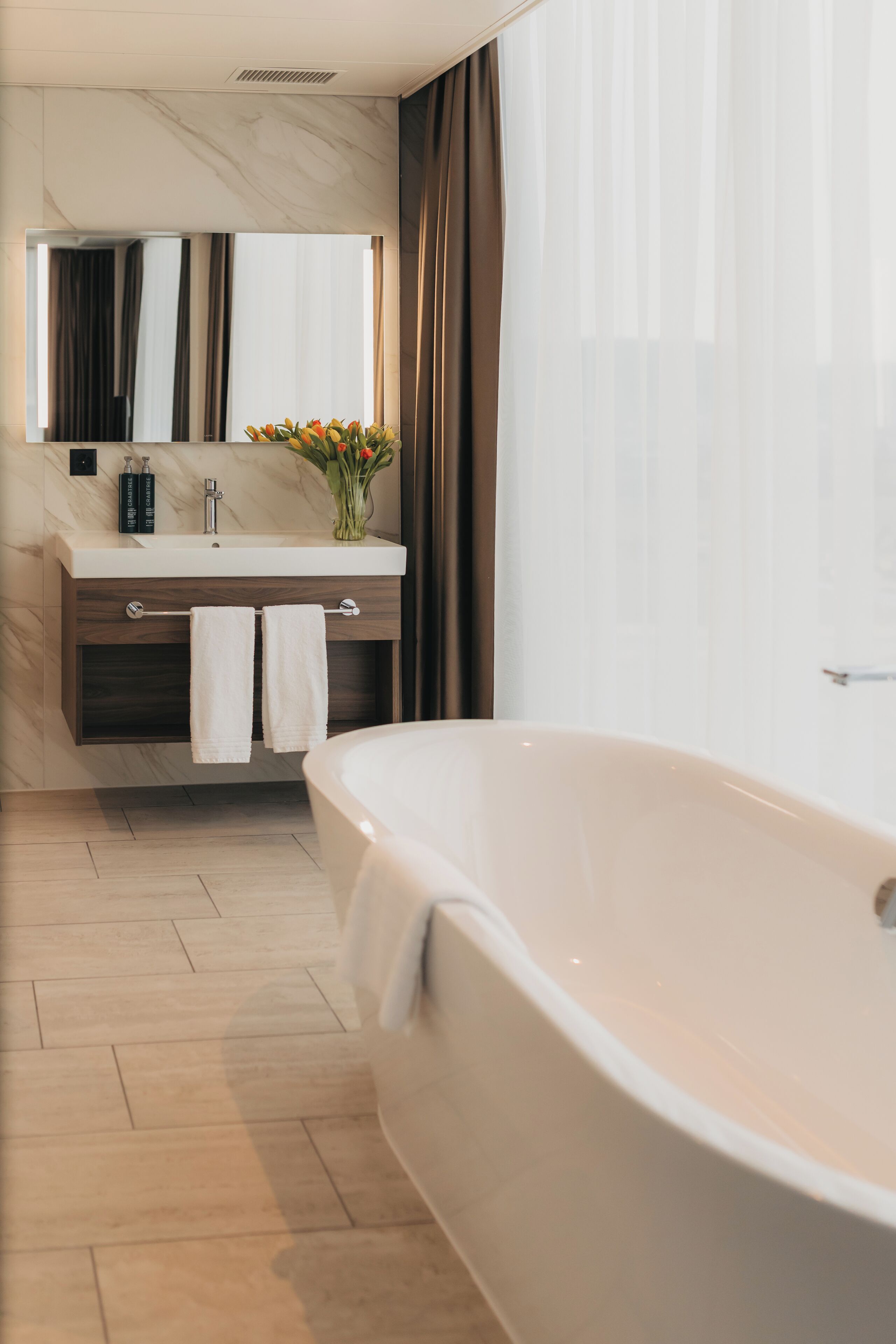 Un bagno moderno con una vasca freestanding, un mobile vanità con specchio e un vaso con fiori.