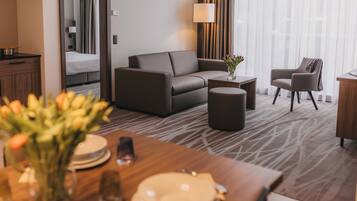 Quarto de hotel moderno com sofá, poltrona, mesa de jantar posta para dois e vista do quarto vizinho.