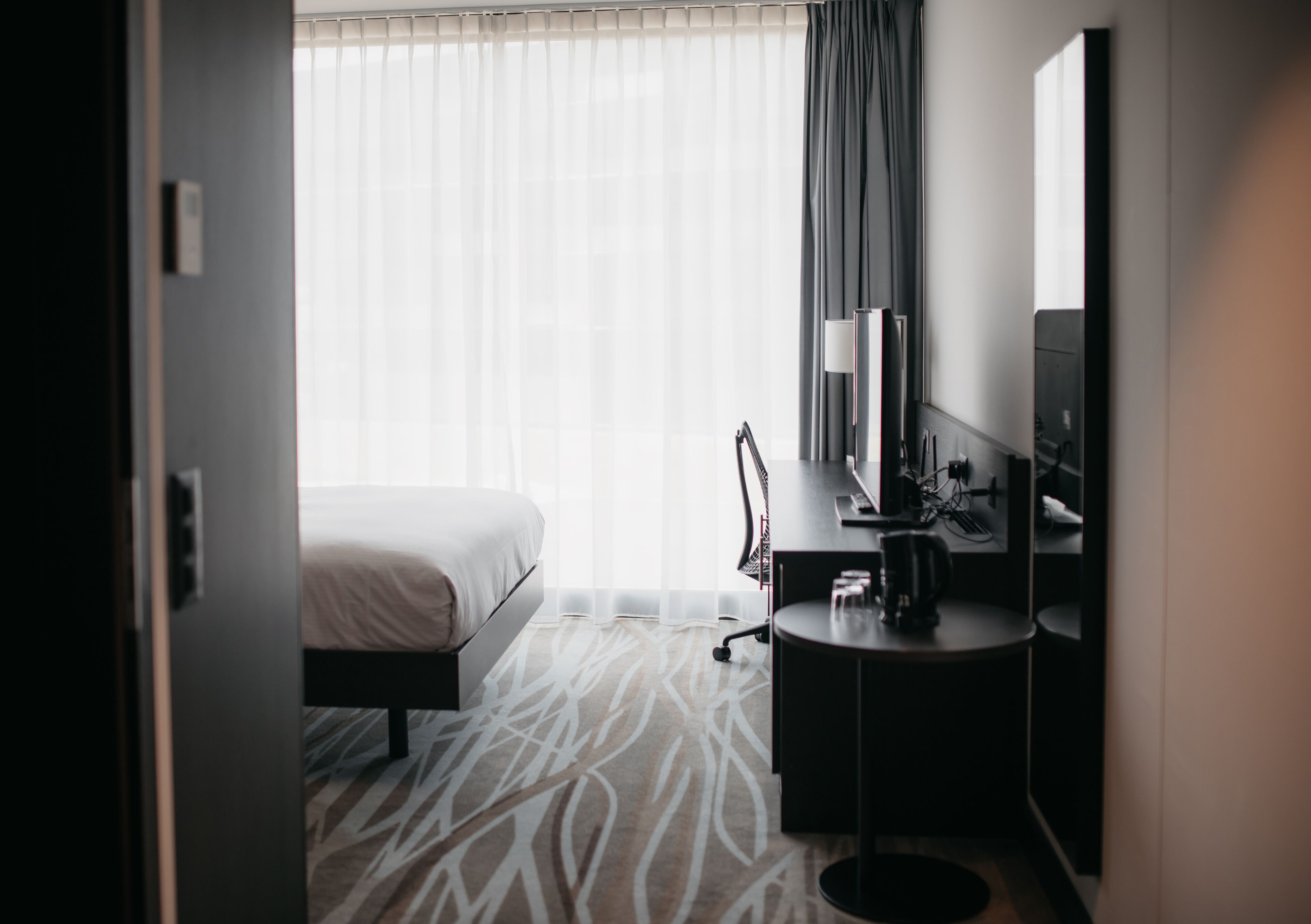 Ein Hotelzimmer mit Bett, Schreibtisch mit Stuhl, Lampe und Fernseher.
