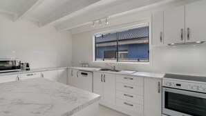 Une cuisine moderne avec des meubles blancs, un plan de travail en marbre, un four encastré et une fenêtre donnant sur l’extérieur.